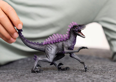 Shadow Raptor toy figure with sharp teeth, claws, and purple spikes, held by a hand on a gray surface.