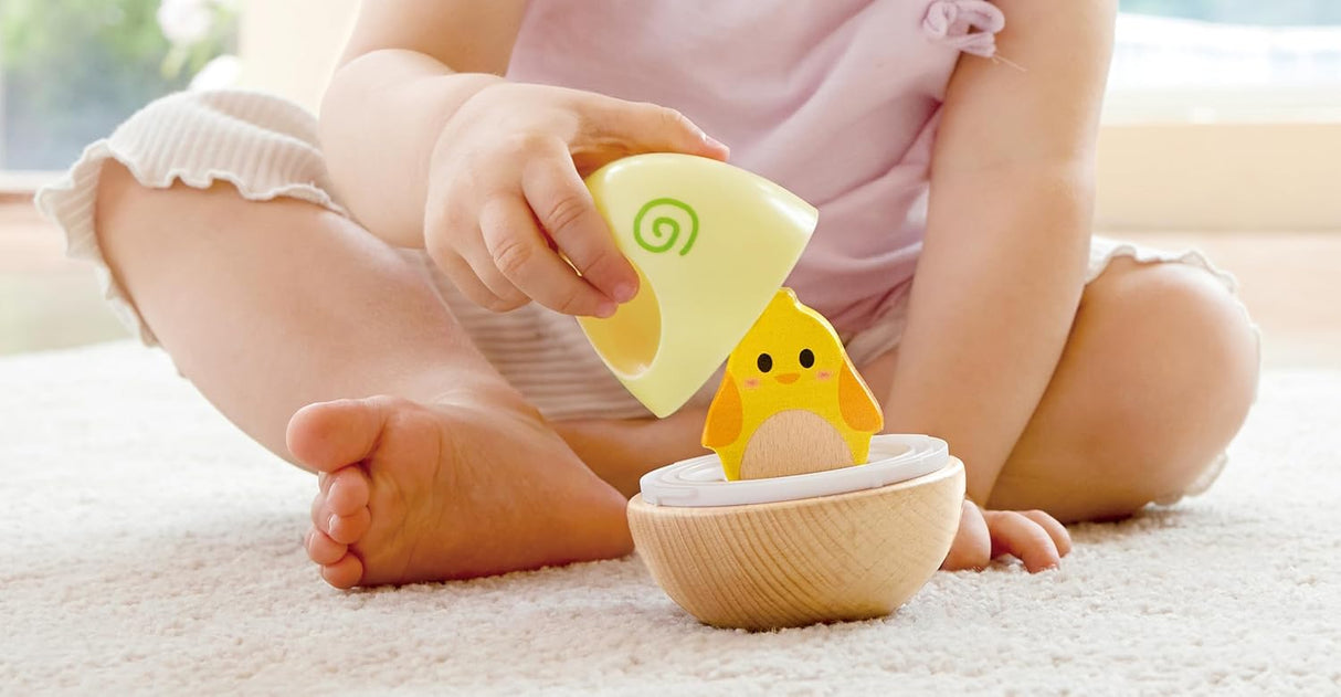 Toddler playing with colorful wobble stacker toy revealing a hidden chick inside wooden base on carpet