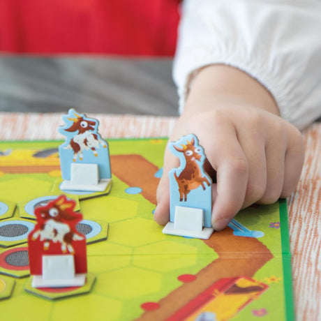 Child's hand moving a game piece on the boardgame in Bouncin' Billy Goats, a fun strategy game for ages 5 and up.