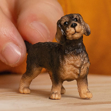 Wire-Haired Dachshund figurine with detailed fur and lifelike features, held by hand on a wooden surface.