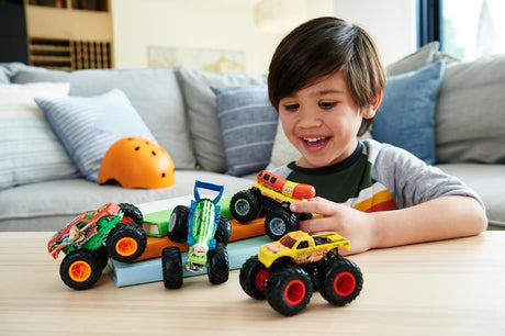 Child happily playing with Hot Wheels Monster Truck 4pk featuring colorful 1:64 scale trucks with giant wheels on a wooden table.