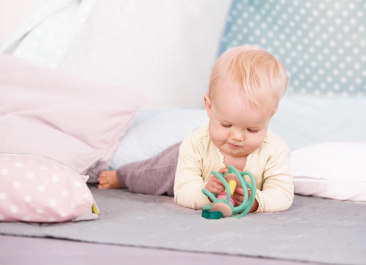 Baby playing with an apple-shaped grab toy made of smooth wood and soft silicone bars, safe for chewing and easy to attach.