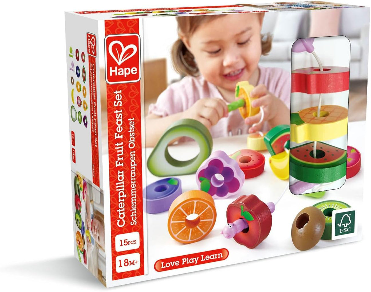 Child playing with colorful wooden caterpillar and fruit threading toy set on white surface