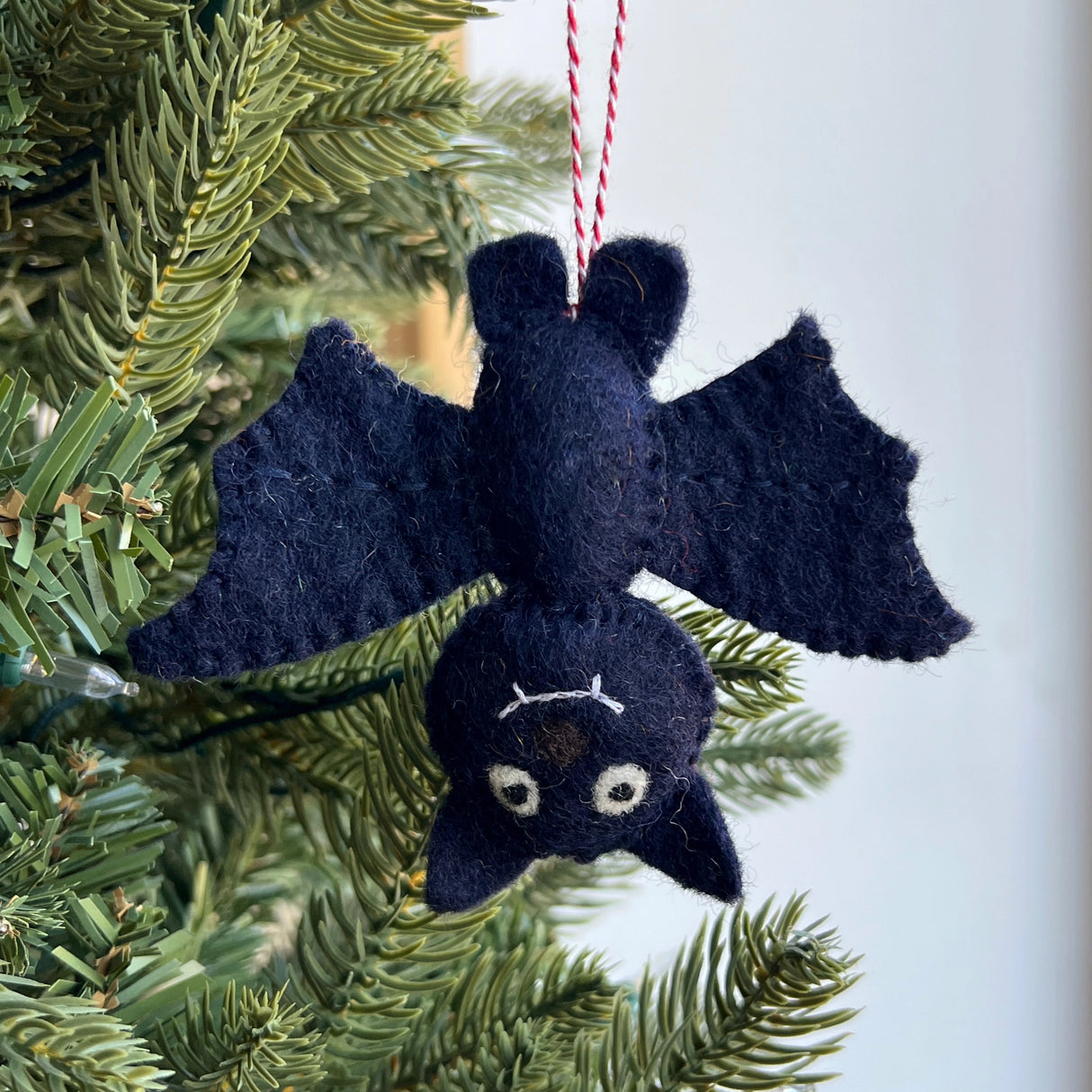 Handmade black felt bat ornament hanging upside down on Christmas tree branch with red and white string