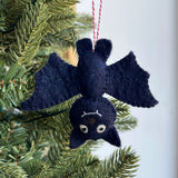 Handmade black felt bat ornament hanging upside down on Christmas tree branch with red and white string