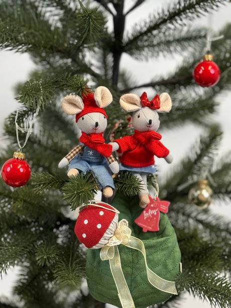 Two festive tiny mice in red sweaters and hats sitting on a Christmas tree branch with ornaments nearby