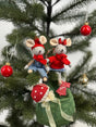 Two festive tiny mice in red sweaters and hats sitting on a Christmas tree branch with ornaments nearby