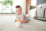 Baby in striped outfit playing with a rolling egg toy that reveals a chick, stimulating motor skills and visual tracking