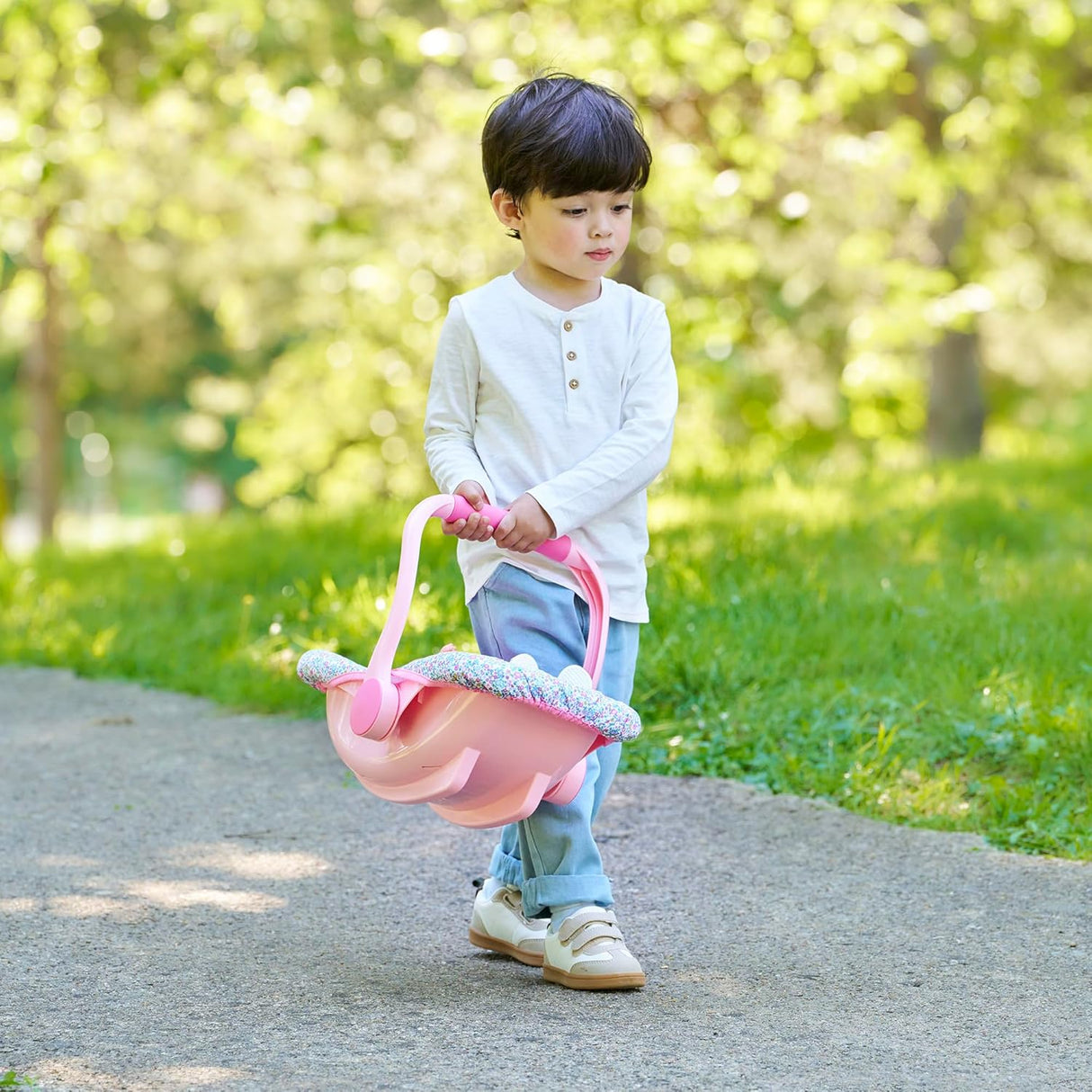 Young child walking outside carrying a pink floral doll car seat carrier with secure straps for imaginative play