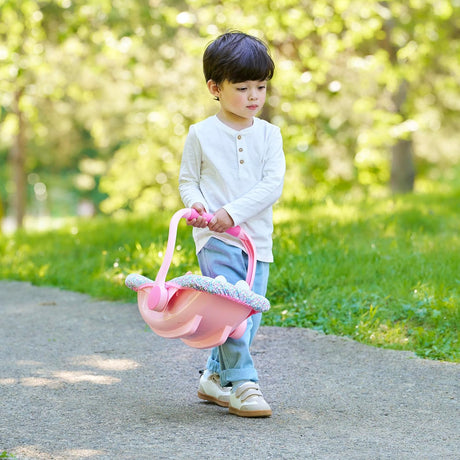 Young child walking outside carrying a pink floral doll car seat carrier with secure straps for imaginative play
