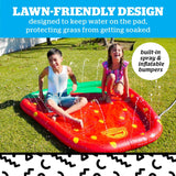 Two kids playing and splashing water on an inflatable red splash pad with built-in sprinklers on grass