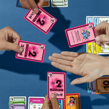Hands playing Monopoly Deal Disney Stitch edition with colorful action and money cards on blue table.