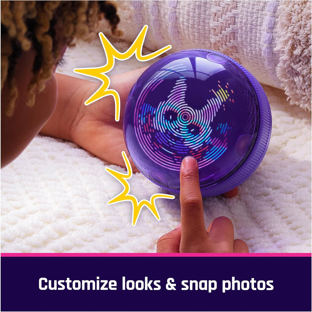 Child’s hand touching a glowing purple Bitzee Hamsterball with colorful interactive lights on a soft blanket surface