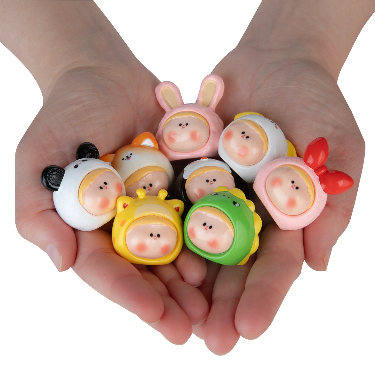 Hands holding seven small collectible baby figures wearing colorful animal and character costumes with smiling faces