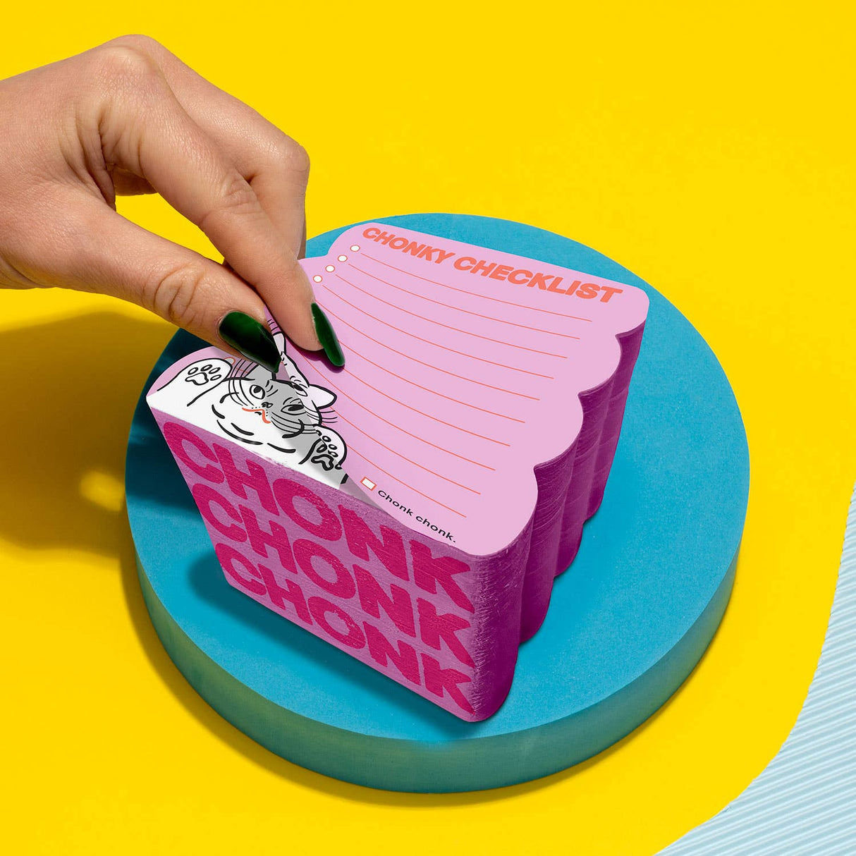 Hand peeling sheet from a chonky pink notepad with scalloped edges and cute tiger illustration on blue round platform