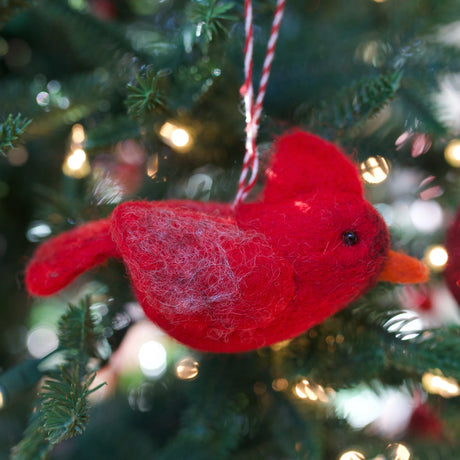Handmade red felt bird ornament hanging on a Christmas tree with festive lights in the background