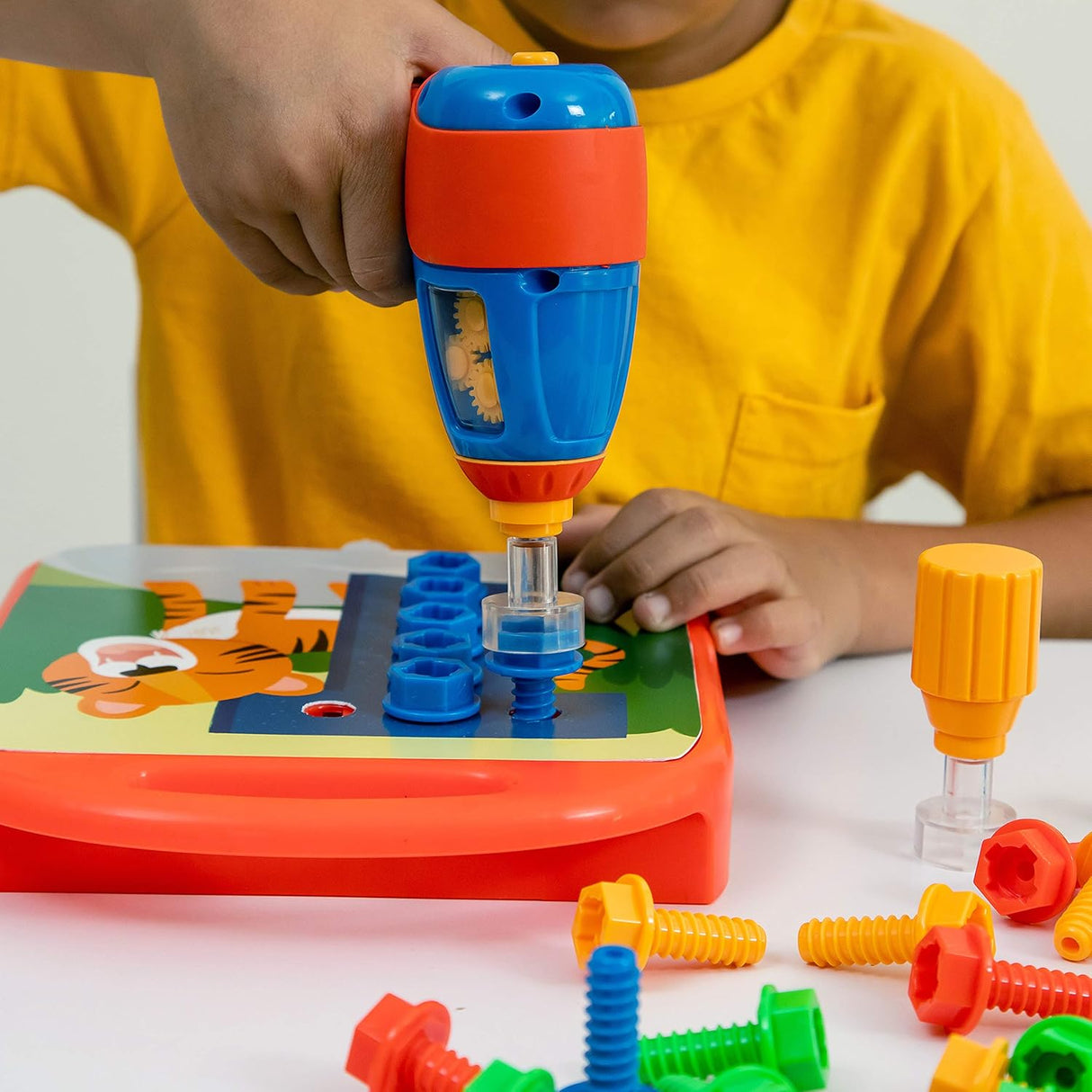 Child using a colorful toy drill to fasten bolts onto a learning board with alphabet and numbers designs
