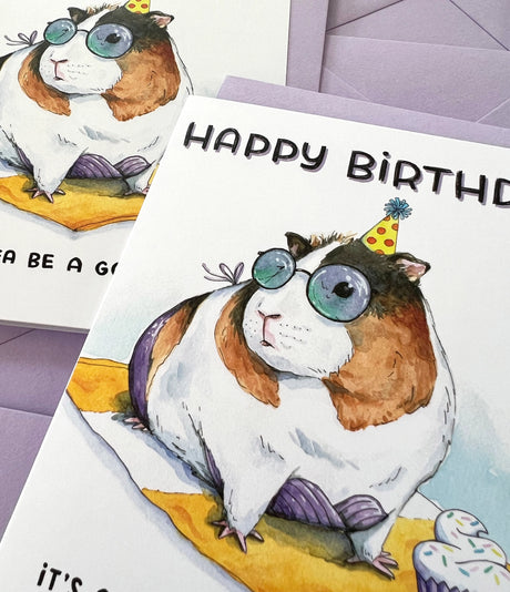 Guinea Pig Beach Birthday Card featuring a watercolor guinea pig with sunglasses and party hat holding a cupcake.