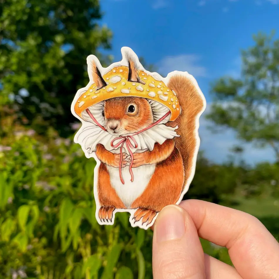 Hand holding Red Squirrel in Mushroom Hat Sticker outdoors with blue sky and green trees background.