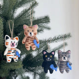 Handmade felt cat Christmas ornaments in various colors each holding a small blue fish hanging on a pine tree branch
