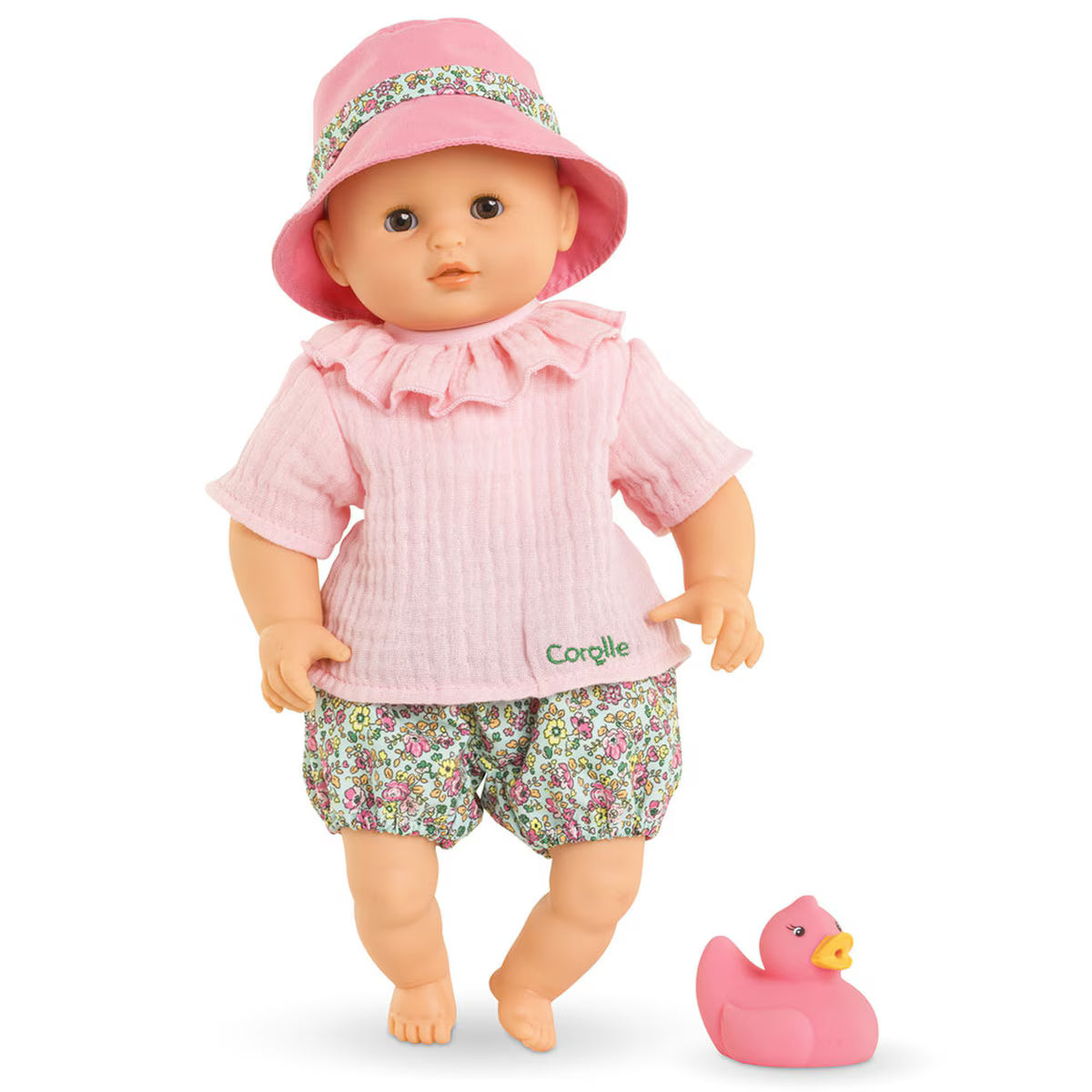 Baby doll wearing pink ruffled top and floral bloomers with matching hat standing next to a pink rubber duck toy