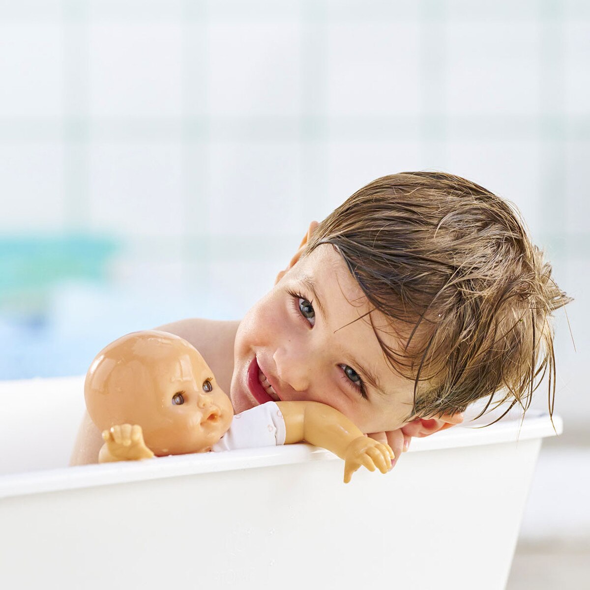 Young child smiling in bathtub holding a doll, enjoying water play and bath time fun