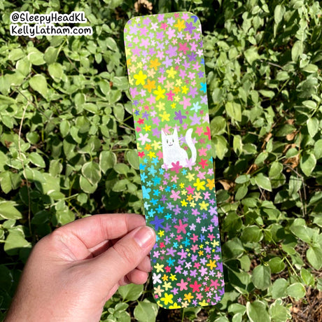 Hand holding Cat & Flowers Bookmark featuring a white cat amid colorful flowers on glossy coated paper.