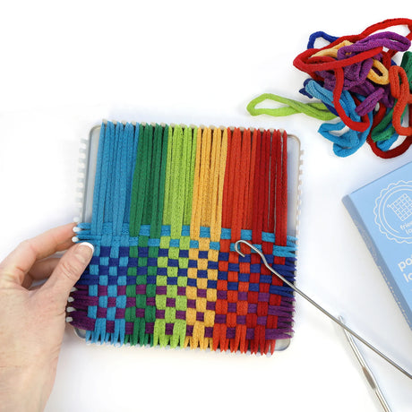 Hand weaving colorful cotton loops on a sturdy metal potholder loom with weaving hooks and extra loops nearby