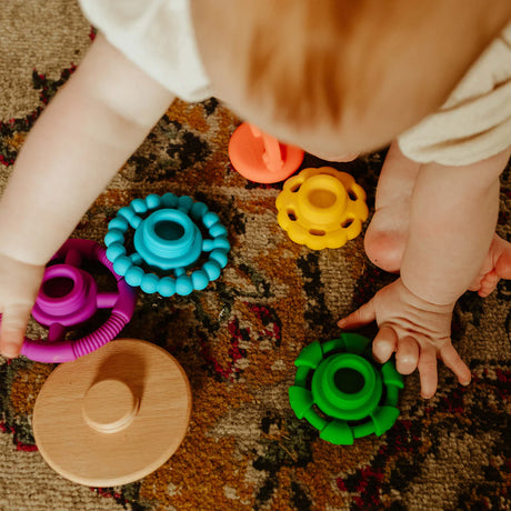 Baby playing with colorful Rainbow Stacker Teether & Toy pieces on patterned carpet floor