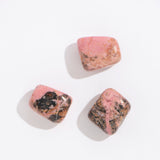Three polished pink and black stones on a white background, Rock | Tumbled Rhodonite gemstone pieces.