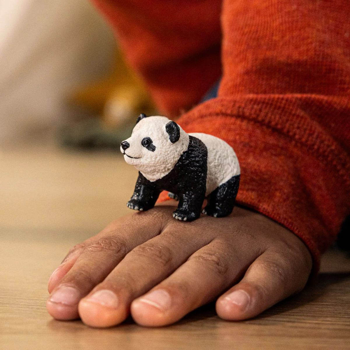 Small textured panda cub figurine standing on a child's hand with a cozy orange sweater in the background