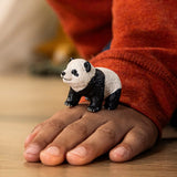 Small textured panda cub figurine standing on a child's hand with a cozy orange sweater in the background