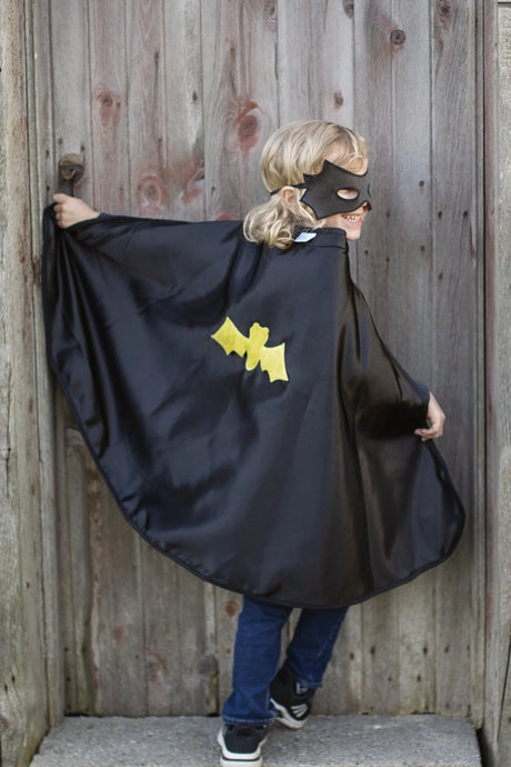 Child wearing Spider Bat Reversible Cape & Mask Size 4-6 showing black satin cape with yellow bat emblem outside.