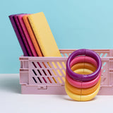 Speks. Helix. Plasma. magnetic fidget coils in purple, pink, and yellow stacked next to colorful notebooks in a pink crate.