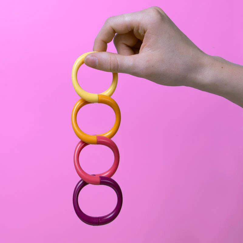 Hand holding colorful connected rings against pink background, magnetic fidget toy Speks. Helix. Plasma.