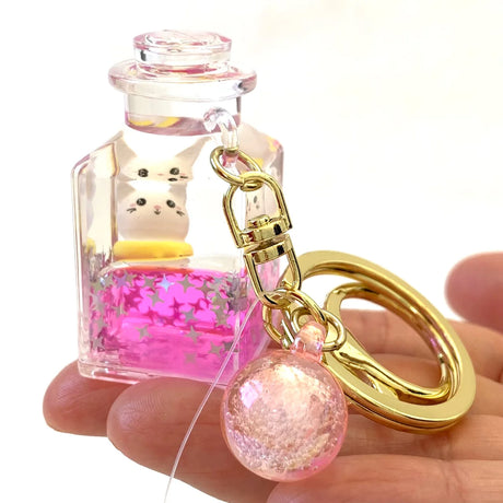 Kitty Jar Floaty KeyChain with clear bottle, pink glitter, and gold keyring held in hand, colorful and cute accessory.