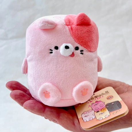 Marshmallow Cat plush toy in pink with silly face and toe bean details held in hand, colorful and adorable.