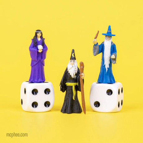Three small wizard figurines in purple, black, and blue robes on dice, Itty Bitty Wizards product image.