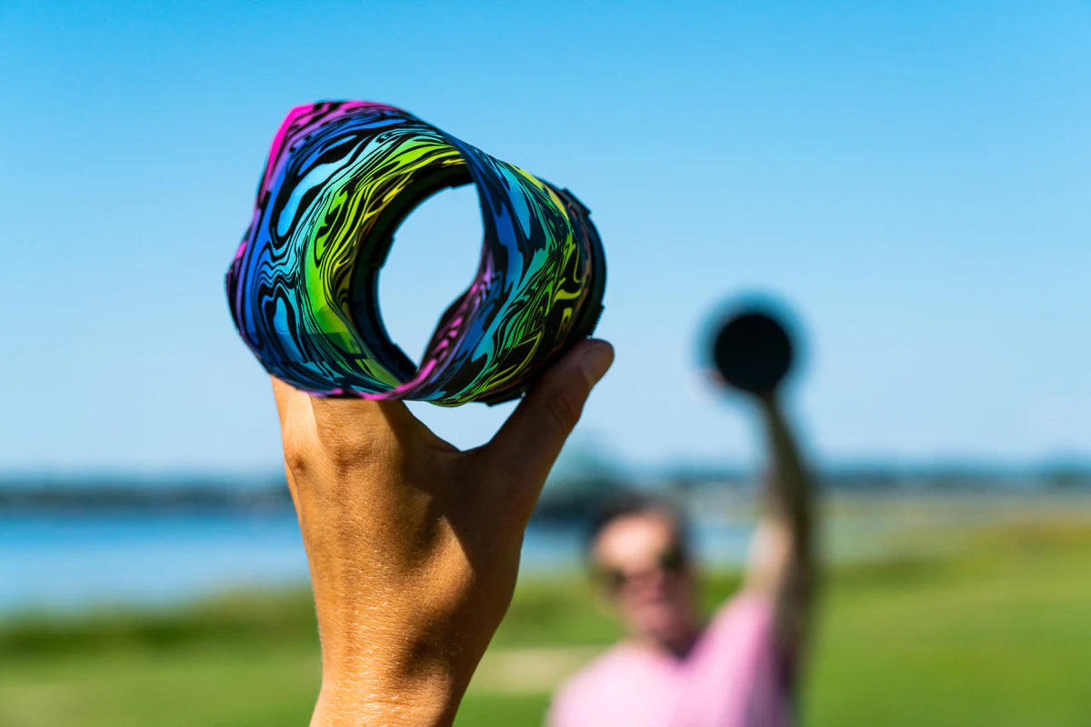 Waboba Throwback showing hand holding colorful AIRLYFT glider with person throwing velcro paddle outdoors.