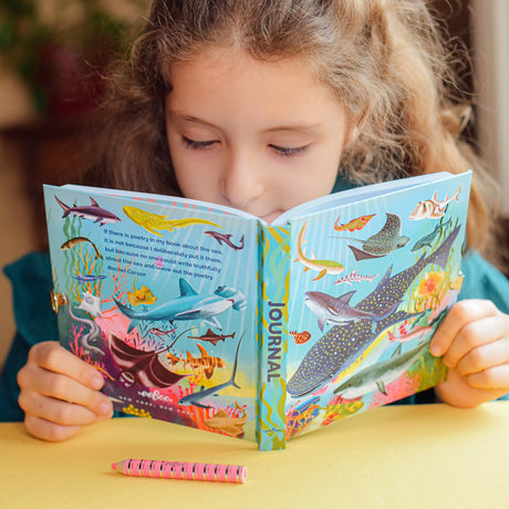 Young girl reading the colorful Sharks & Friends Diary with vivid sea creature illustrations and foil stamped cover.