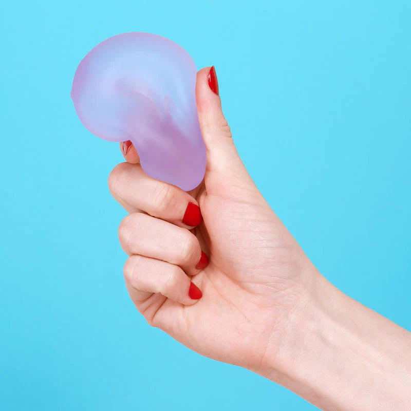 Hand holding a soft, purple gel stress loop against a bright blue background with red nail polish on nails