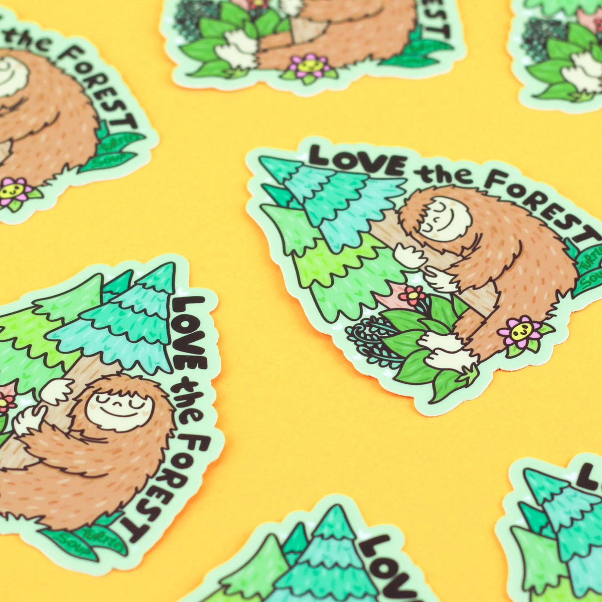 Love the Forest Bigfoot Sticker showing a friendly Bigfoot hugging a tree surrounded by forest plants on a yellow background.