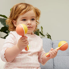 A child holding orange and yellow Maracas musical shakers while seated on a sofa