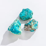 Three rough chrysocolla stones with vibrant blue-green hues on a white background, Rock | Rough Chrysocolla product.