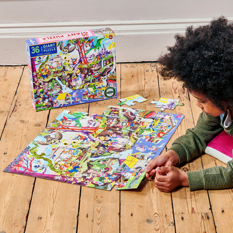 Child assembling the colorful 36pc Fairies & Tales Giant Puzzle on wooden floor with box nearby.