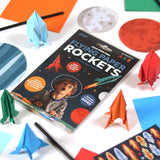 Flying Paper Rockets kit with colorful folded paper rockets and space-themed stickers and game pieces on a table