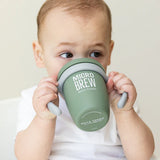 Baby holding and drinking from a green silicone Happy Sippy Cup with easy-grip handles and Micro Brew branding