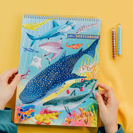 Hands holding Shark Sketchbook with colorful shark and sea creatures on cover, spiral-bound for sketching.
