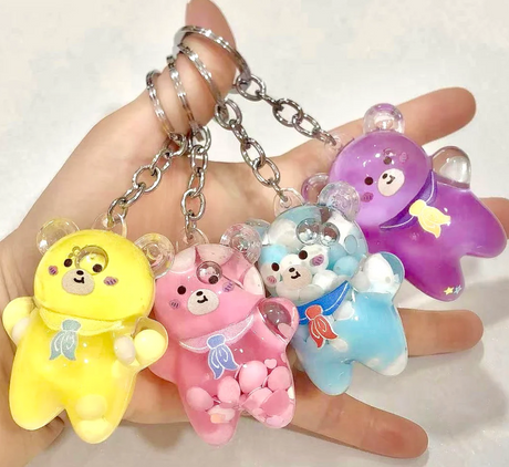 Hand holding four colorful Bear Floaty Charm Keychain in yellow, pink, blue, and purple with silver keyrings.