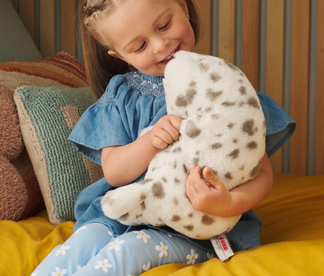 Child hugging Snuffles Leopard Seal Nuri soft plush toy with white-gray spotted design and big smile.